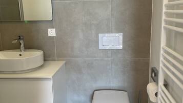 A modern bathroom with a white sink, a toilet, and a trash bin.