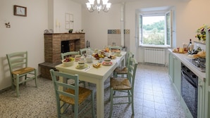 Uma sala de jantar com lareira, janela com vista e bancada de cozinha com alimentos.