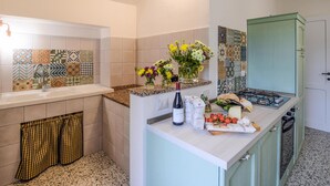 Uma cozinha com fogão a gás, pia e diversos azulejos decorativos. Há flores no balcão e uma garrafa de vinho.