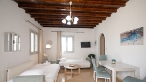 A modern hotel room with a wooden ceiling, a white bed, a round dining table, and a TV mounted on the wall. - Mykonos Stylish Ivory Apt w Shared Pool (Mykonos)
