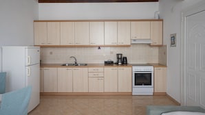 A compact kitchen with light wooden cabinets, a white refrigerator, a stove, and a sink. - Mykonos Stylish Ivory Apt w Shared Pool (Mykonos)