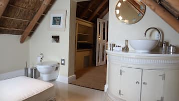 Bathroom features a classic design with a white vanity, pedestal sink, and toilet, set against a tiled floor and wooden ceiling.