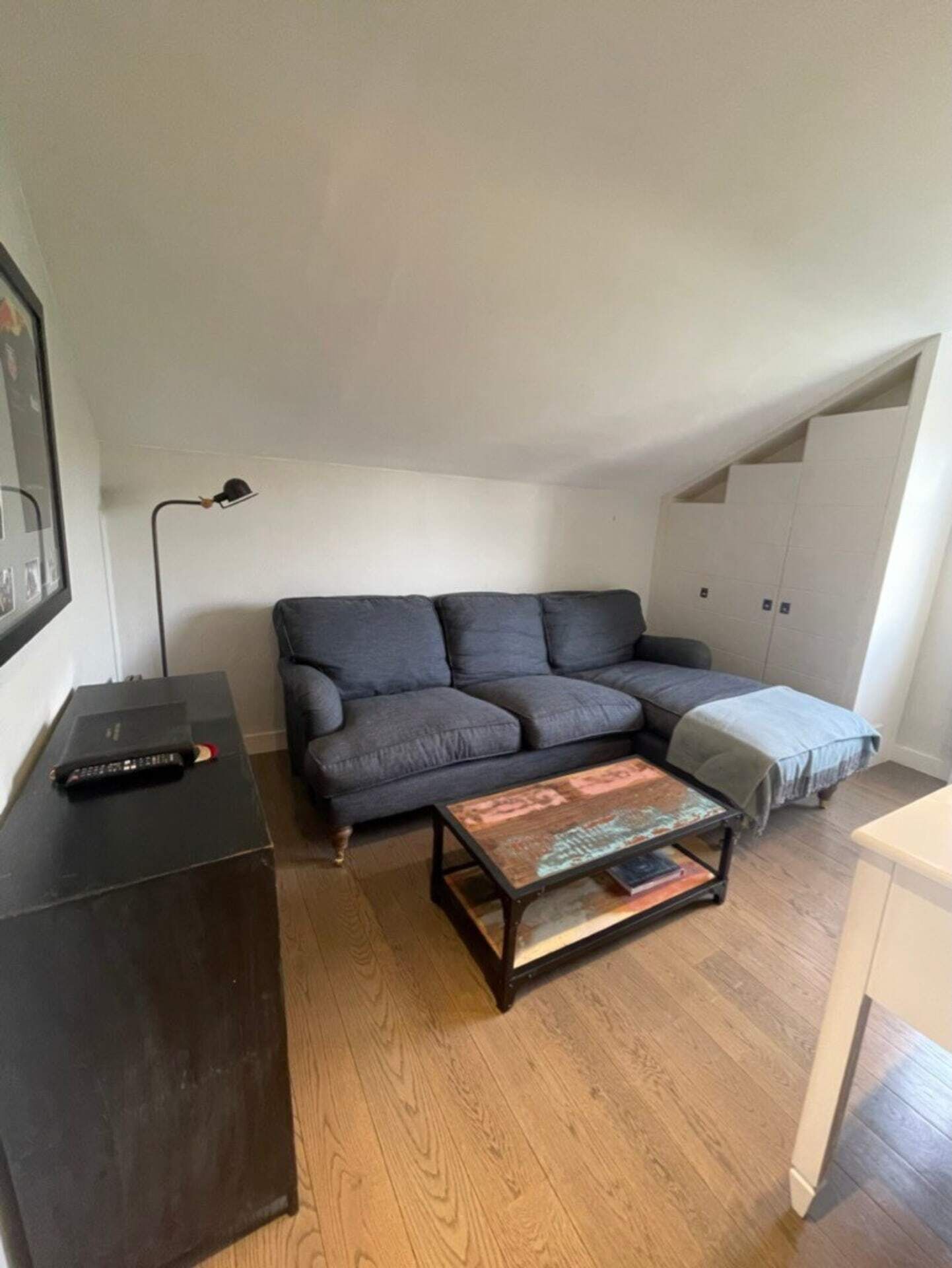 A small, cozy living room with a dark grey sofa, a wooden coffee table, and a black TV stand.