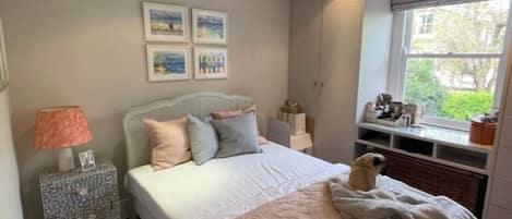 A bedroom with a bed, bedside table, lamp, and wall art.