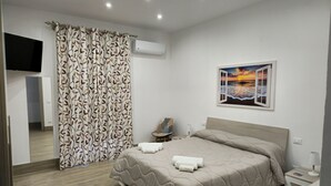 A modern bedroom with a bed, a nightstand, a TV, and a painting of a sunset.