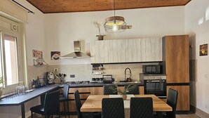 A modern kitchen with a central island, black chairs, a wooden dining table, and a hanging light fixture.