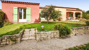A two-story house with a stone wall in front, a grassy yard, and a patio with outdoor furniture. - Beautiful home in Mazan with WiFi (Mazan)