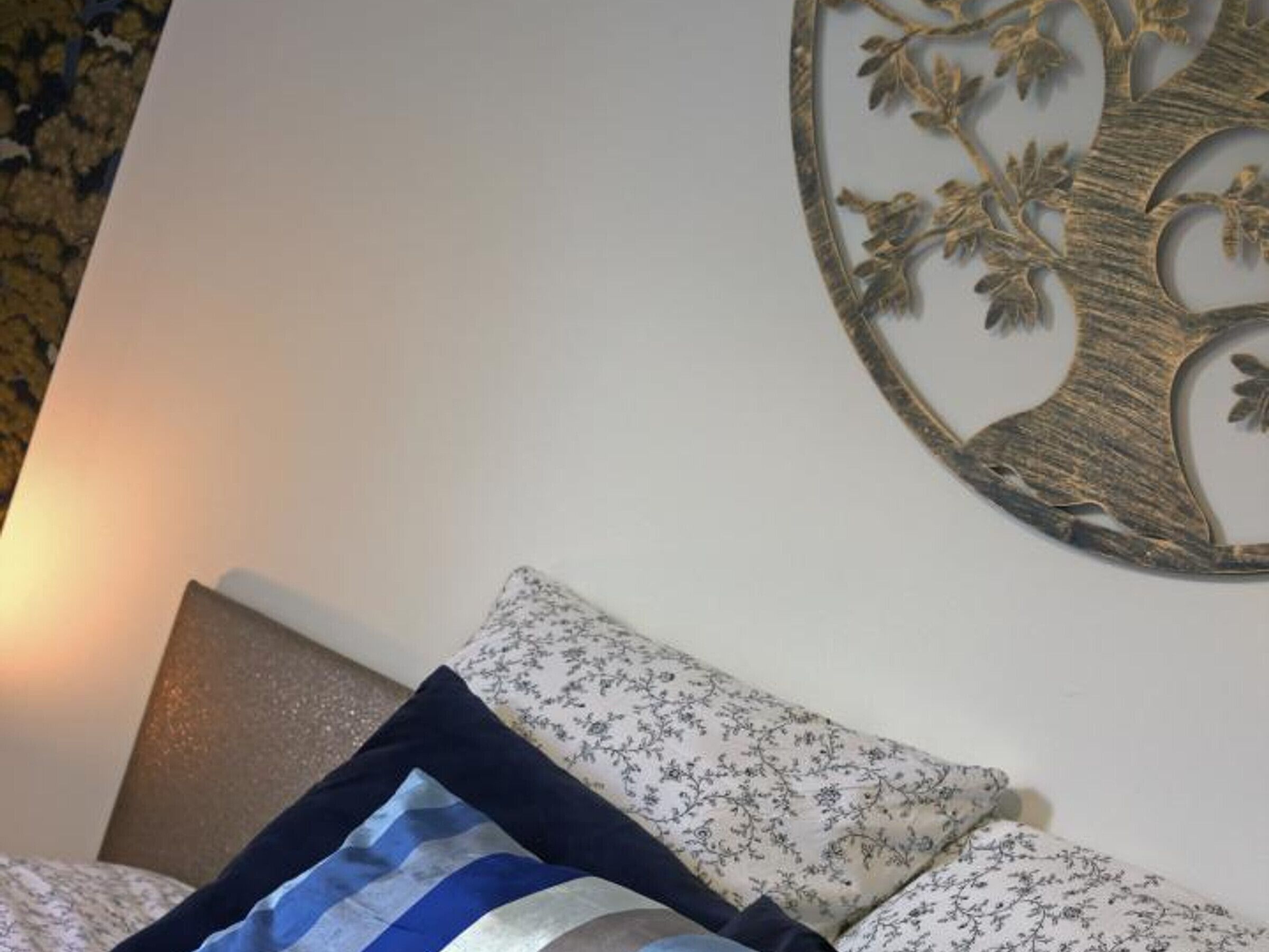 Ein Bett mit einem blumengemusterten Kopfteil und einem dekorativen Wandbild von einem Baum.