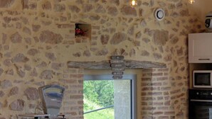 Une cuisine rustique avec des murs en pierre, un plan de travail en bois, un four encastré et une vue sur la verdure à l’extérieur.
