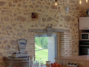 Une cuisine rustique avec des murs en pierre, un plan de travail en bois, un four encastré et une vue sur la verdure à l’extérieur.