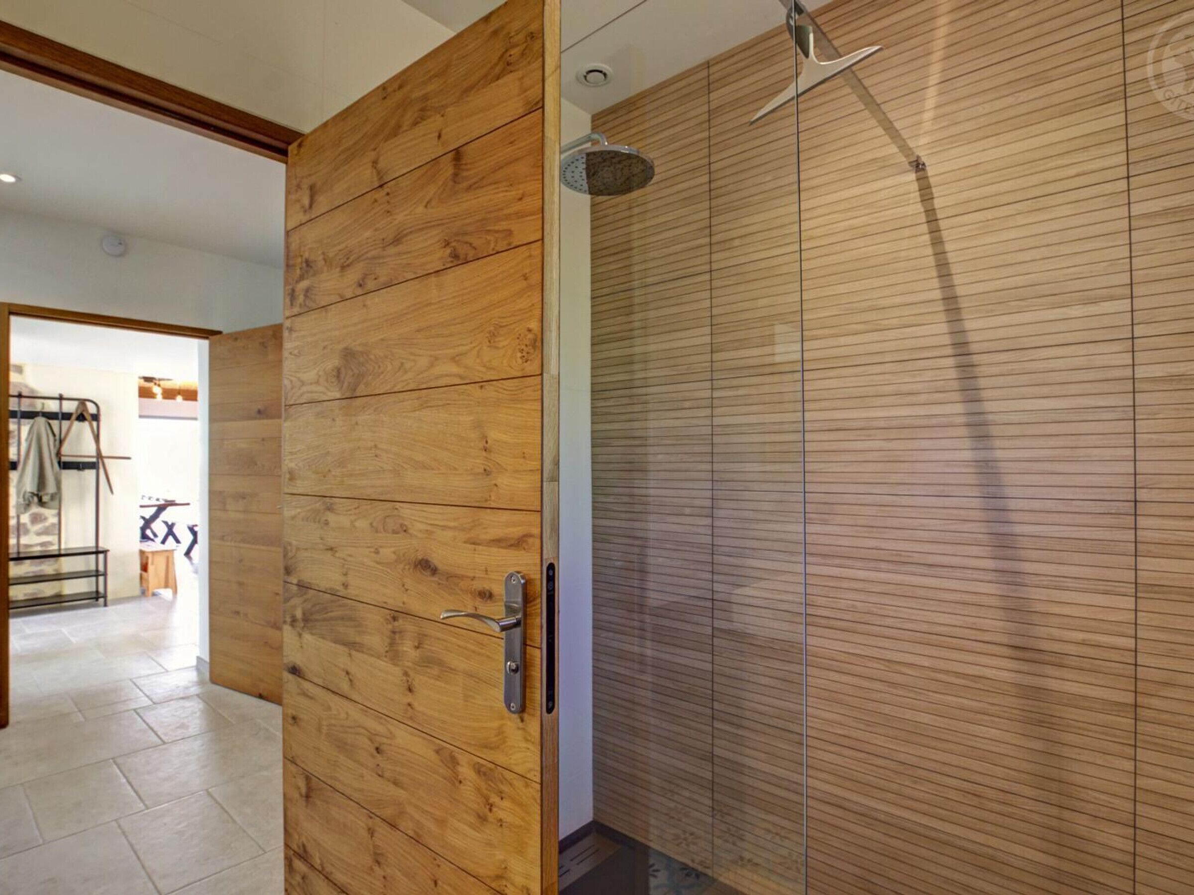 A wooden door leading to a bathroom with a shower.