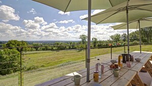 Un espace de restauration en plein air avec des tables de pique-nique, des parasols et une vue panoramique sur un paysage rural.