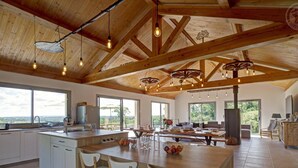 Une cuisine spacieuse dotée d’un grand îlot central, de poutres en bois et offrant une vue sur l’extérieur.