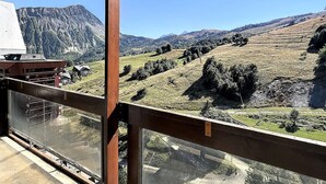 Un balcon donnant sur un paysage montagneux, un bâtiment doté d’un toit en pente et un ciel d’un bleu limpide.