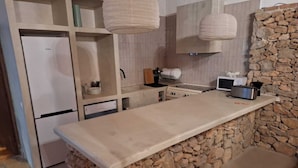 A kitchen with a stone accent wall, a built-in stove, and hanging light fixtures. - Bakit House - Casa Rural con Piscina Privada (Águilas)
