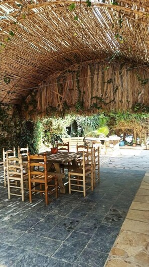 Relax in a shaded outdoor dining area with a thatched roof, surrounded by lush vegetation and comfortable seating.