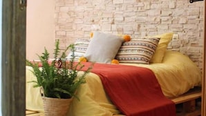 A cozy room with a bed on a wooden pallet, a stone wall, and a hanging lamp. - Bakit House - Casa Rural con Piscina Privada (Águilas)