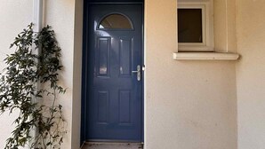Eine dunkelblaue Tür mit einem kleinen Fenster darüber, eine weiße Wand und eine Pflanze links.