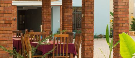 An outdoor dining area with brick pillars, wooden chairs, and tables covered with red tablecloths.