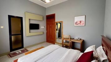 Una habitación de hotel con una cama, un escritorio con silla, un televisor montado en la pared y una puerta que da a otra habitación.