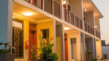 A multi-story hotel with a balcony, large windows, and potted plants.