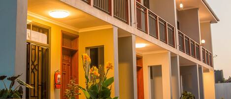 A multi-story hotel with a balcony, large windows, and potted plants.