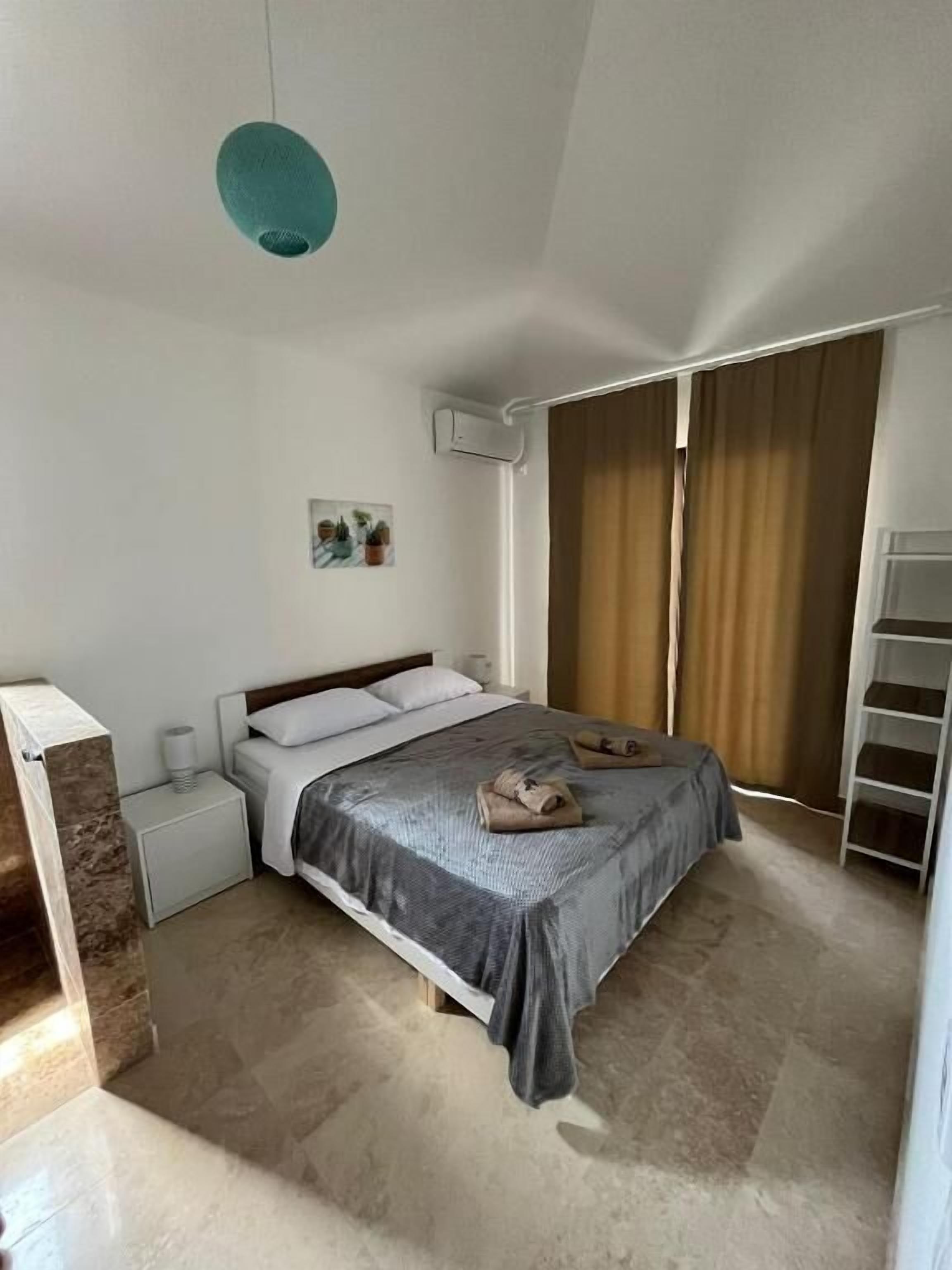 A bedroom with a bed, nightstands, an air conditioning unit, a painting, and a wardrobe.