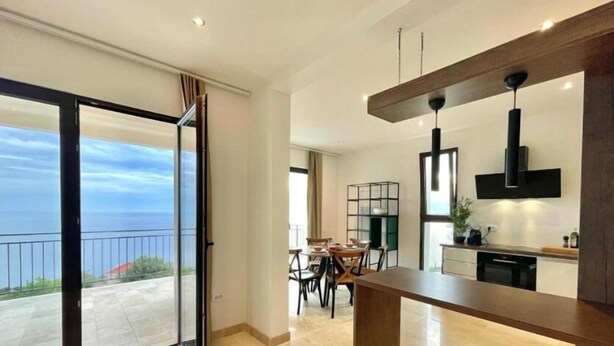 A modern kitchen with a large island, a dining area with chairs, and a view of the sea through a glass door. - Family Vacation Villa Rezevici (Petrovac)