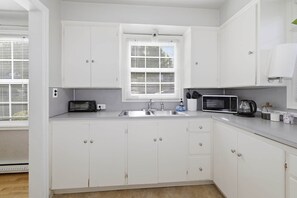 A modern kitchen with white cabinets, a built-in microwave, a toaster, and a sink. - Charming 1930s Style Rustic Home (Eugene)