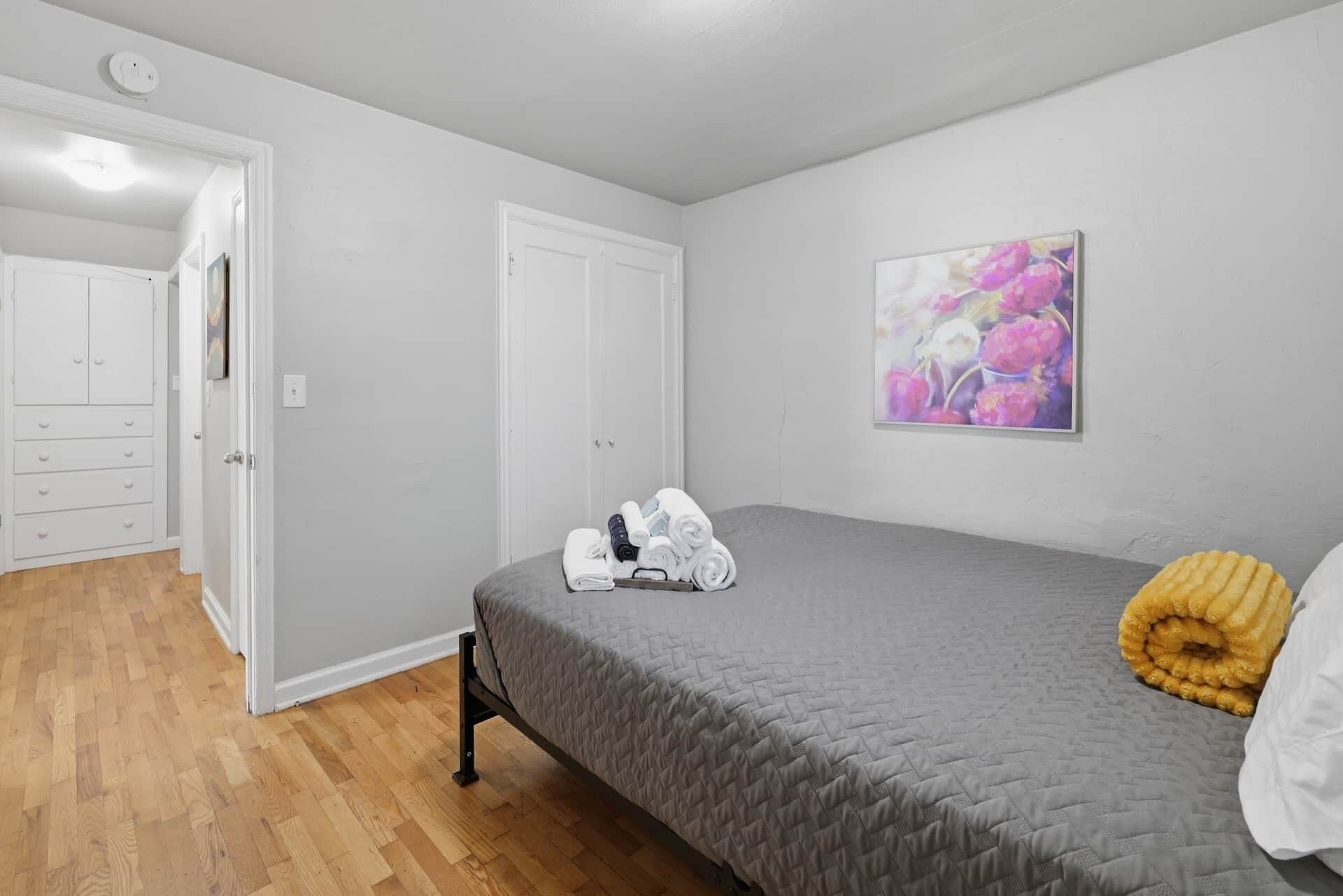 A bedroom with a bed, a door, a painting, and a wooden floor.