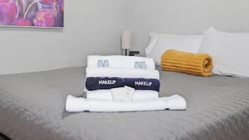 A neatly made bed with a folded towel labeled 'MAKEUP' and a rolled towel on the side.