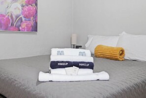 A neatly made bed with a folded towel labeled 'MAKEUP' and a rolled towel on the side. - Charming 1930s Style Rustic Home (Eugene)