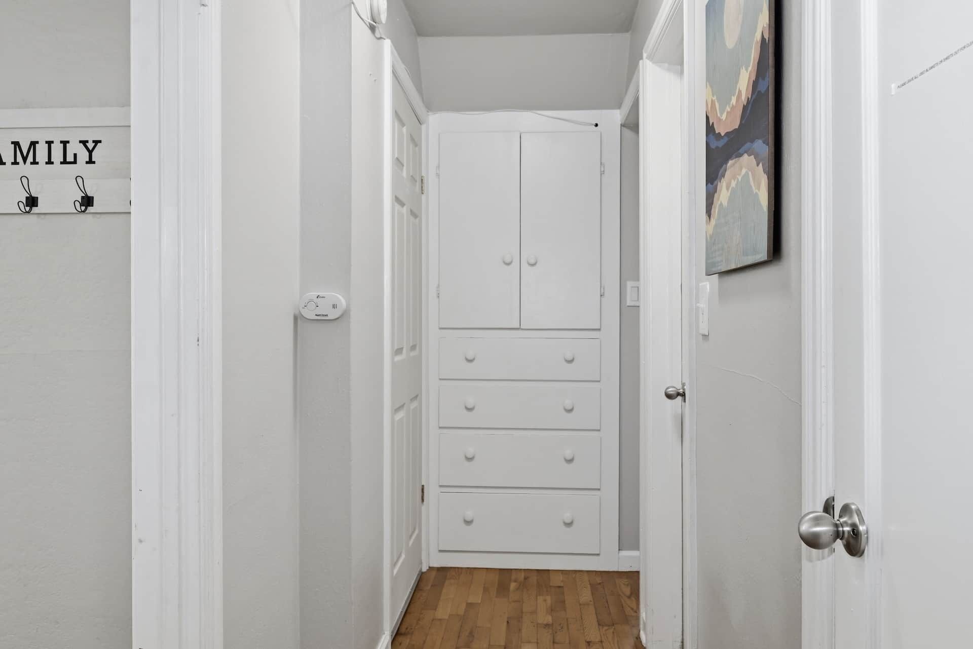 Un pasillo estrecho con una puerta blanca al final que da a una habitación con un armario.