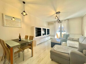 A modern living room with a glass dining table, a sofa, and a TV. - Family Apartment Garden View (Budva)