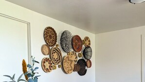 A dining area with a round wooden table, two chairs, a vase with a plant, and a wall decorated with woven plates. - Quiet and Unique 2BR on Winery Row - The Elgin Project (Elgin)