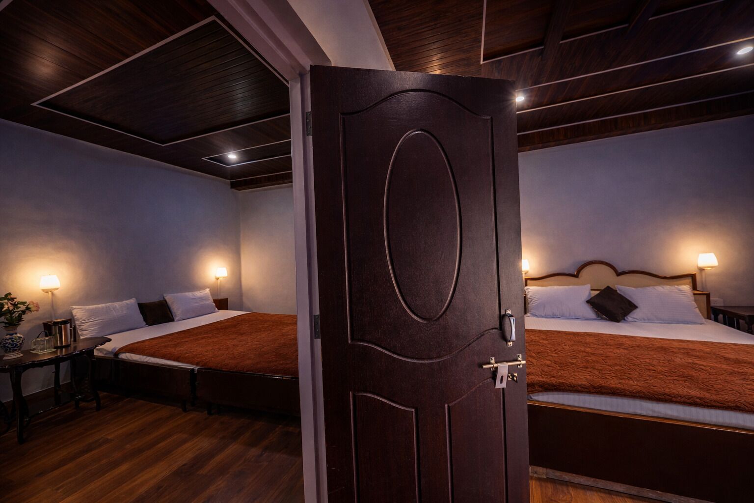 Habitación de hotel con dos camas, piso de madera y una puerta de madera oscura.