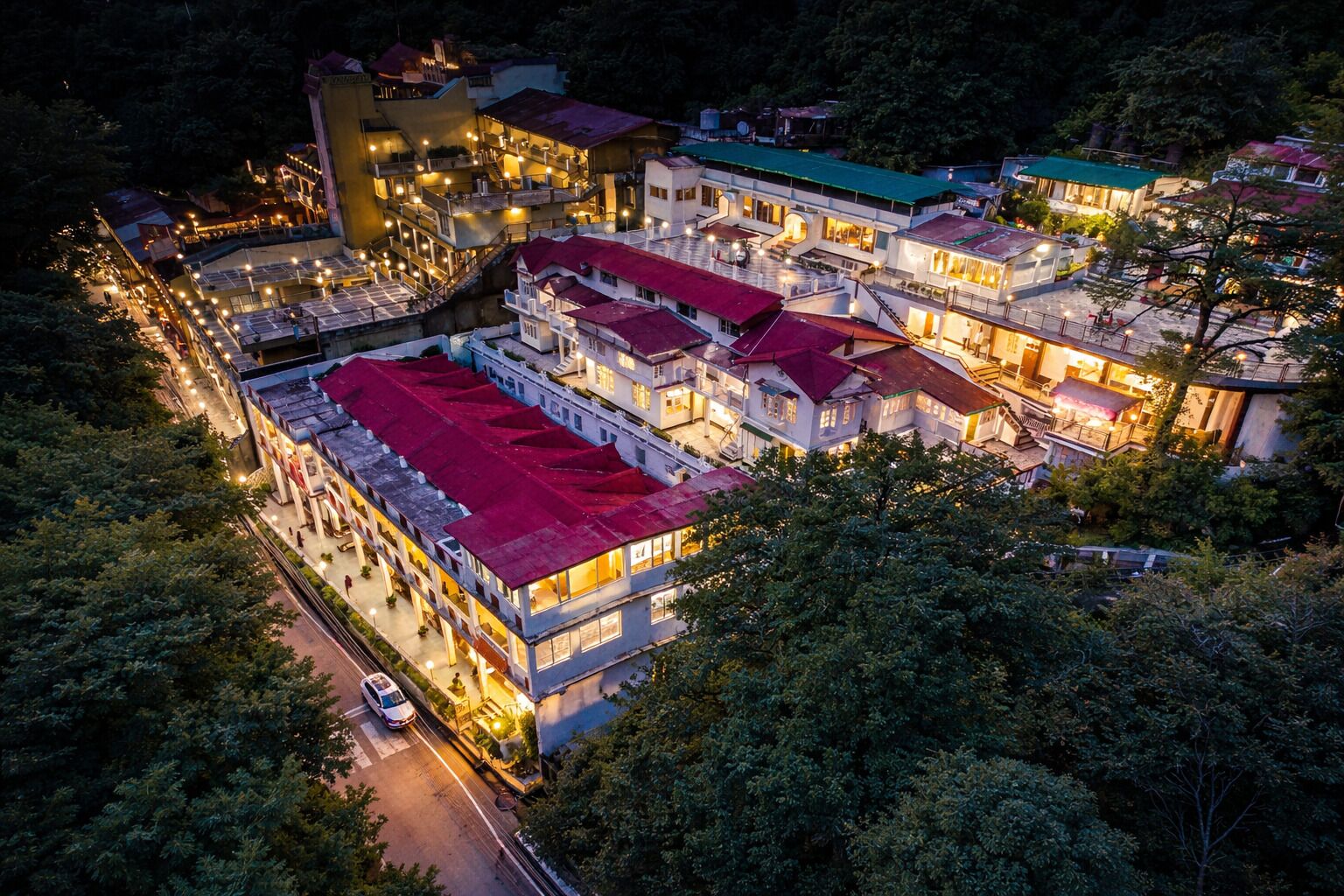 A multi-story hotel with a red-roofed central building, multiple balconies, and a well-lit exterior.