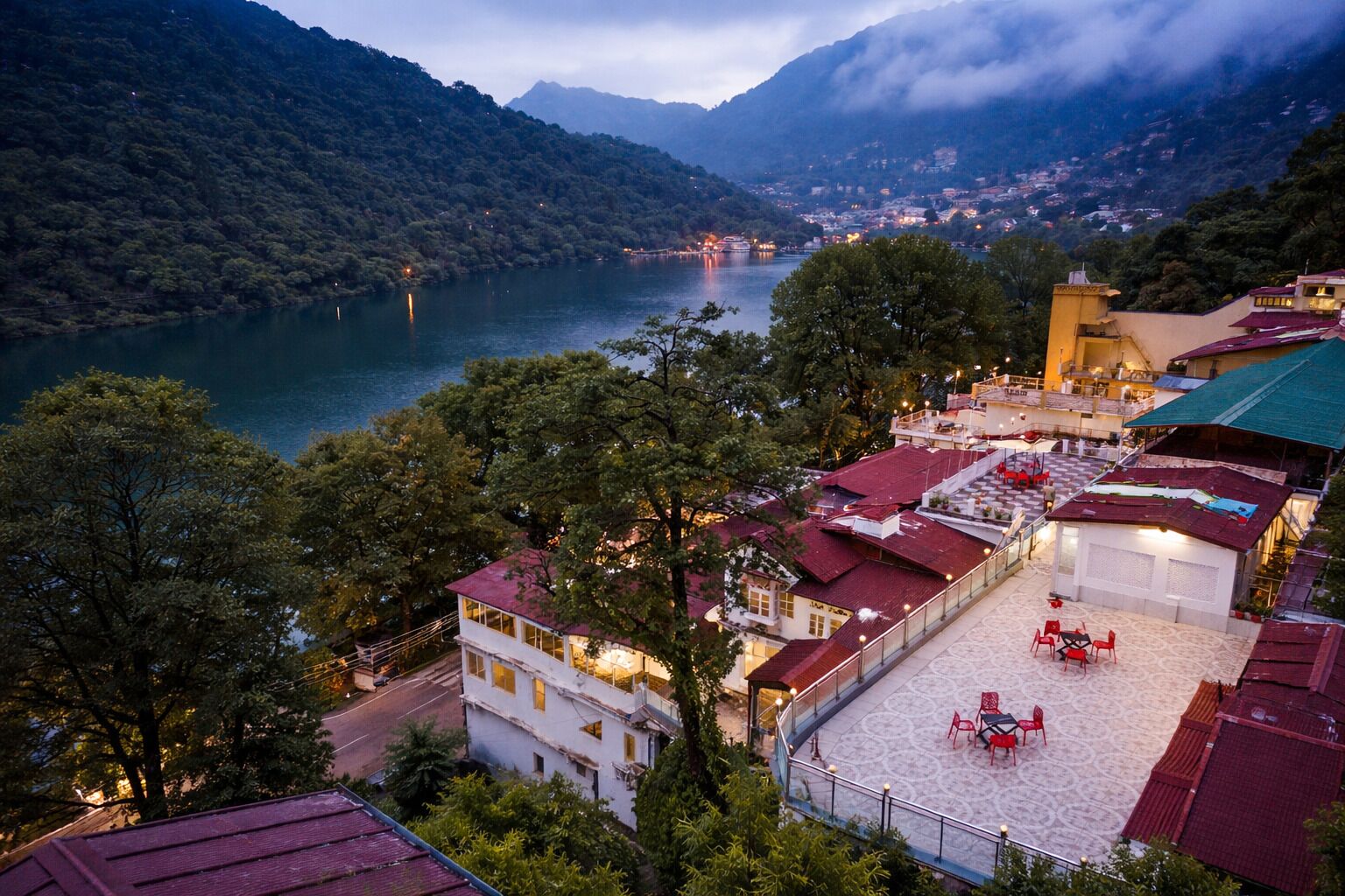 Un hotel con terraza, vistas a un lago y montañas circundantes.