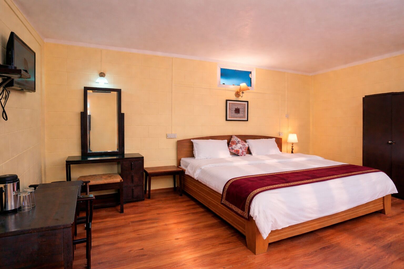Una camera d'albergo con un letto di legno, una scrivania con una sedia, uno specchio e una piccola finestra.