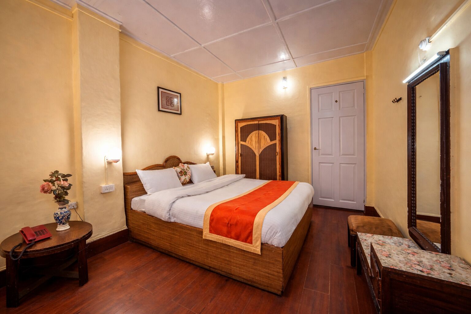 A bedroom with a wooden bed, bedside tables, a nightstand, a mirror, and a door.