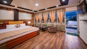 A hotel room with a large bed, a desk, two chairs, a TV, and a view of the cityscape. - India Hotel - Mall Road Nainital - Lake View (Nainital)
