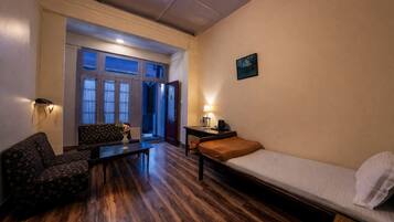 Habitación con cama, sofá, mesa y una silla. Hay una puerta que da a un espacio al aire libre.