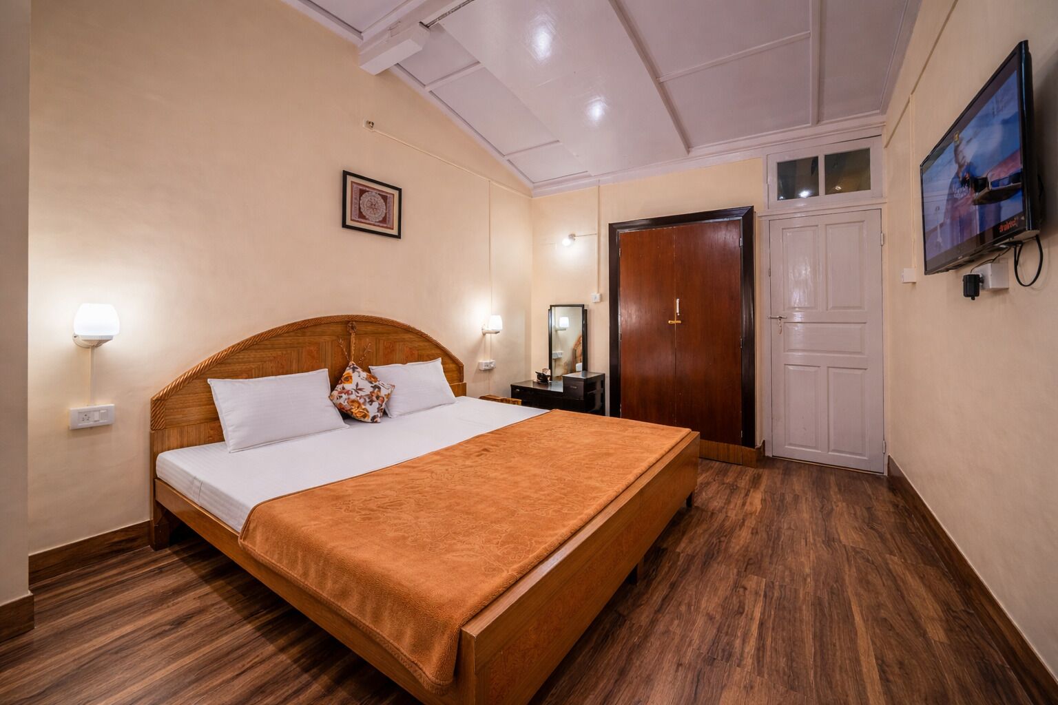 Una habitación de hotel con una cama de madera, una mesita de noche, un espejo, un armario y un televisor.