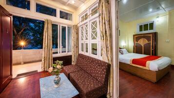 A room with a sofa, a bed, a window with curtains, and a vase with flowers on a table.