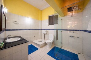 Baño con lavamanos, inodoro y zona de ducha, con una decoración en tonos amarillo y blanco.