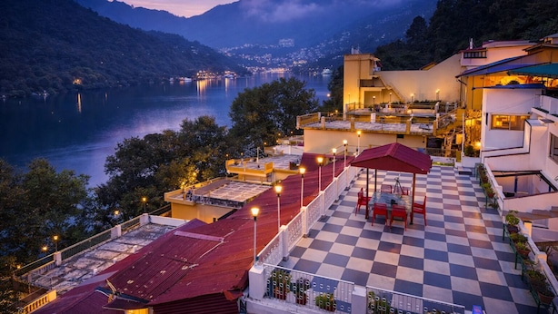 A hotel with a terrace overlooking a lake, featuring a checkered floor and red umbrellas. - India Hotel - Mall Road Nainital - Lake View (Nainital)