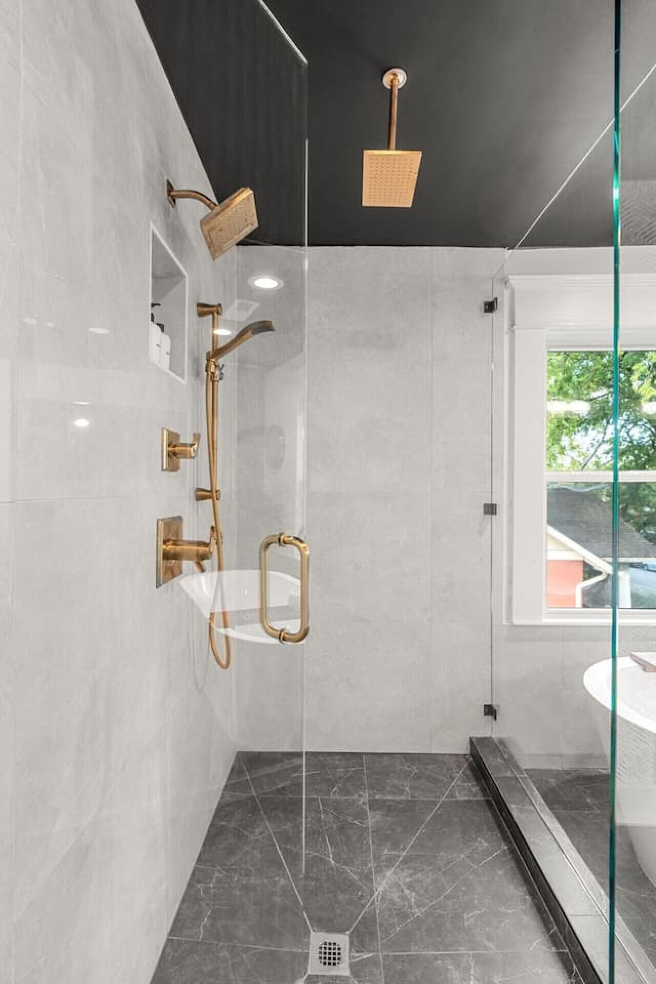 Une salle de bain moderne avec une douche à parois de verre, une pomme de douche dorée et un lavabo blanc.