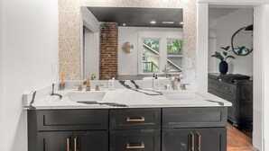 A modern bathroom with a double sink vanity, a large mirror, and a brick accent wall.
