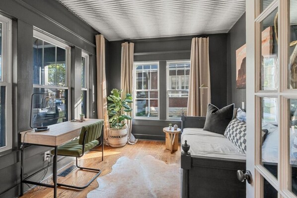 Una habitación acogedora con escritorio, silla, sofá y ventanas amplias.