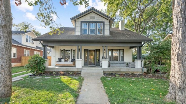 A two-story house with a front porch, a covered entryway, and a small front yard with grass and trees.